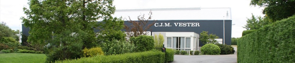 C.J.M. Vester 公司的厂房外景,灰白色长条仓库,墙上有公司名称,前景是修剪整齐的绿篱和草坪